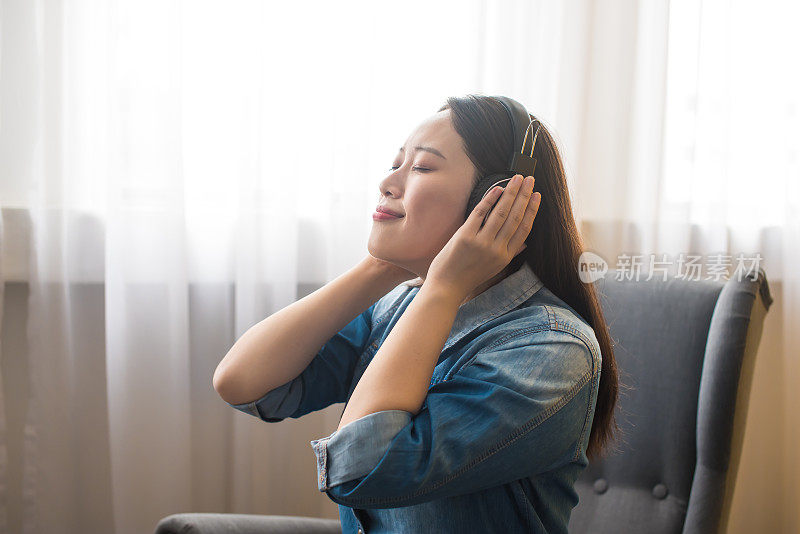 亚洲妇女在行动管制令期间呆在家里，坐在沙发上欣赏音乐，以应对全球大流行的爆发。