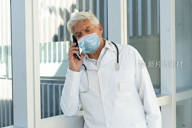 高级医生在医院走廊使用智能手机的肖像。新常态。