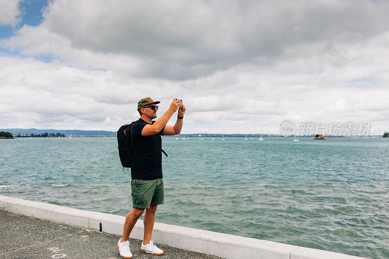 一名男子在海边用手机拍照