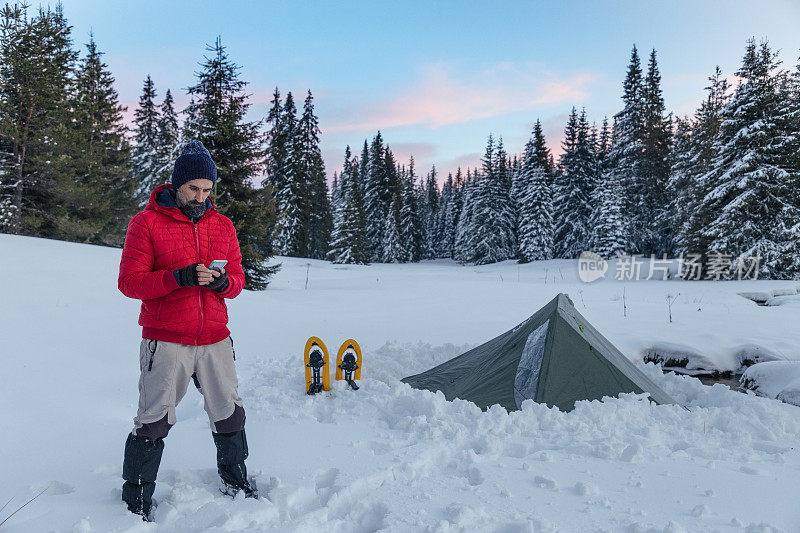 游客在冬季山地露营时在帐篷附近使用手机。在2019冠状病毒病大流行期间，自然是孤独的。心理健康和生活平衡。