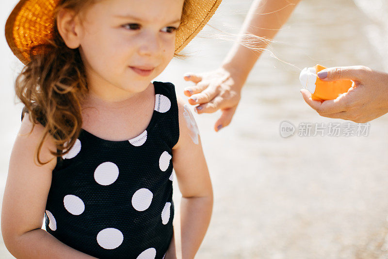 在海滩上，妈妈给小女儿脸上涂防晒霜