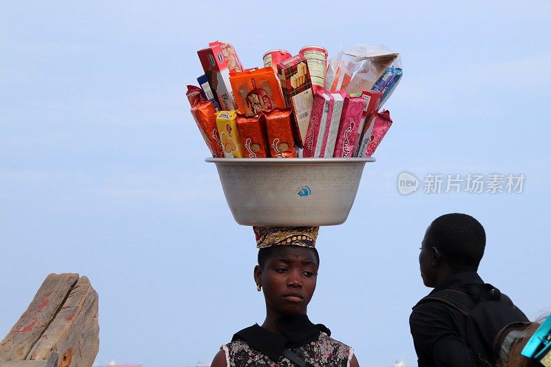 在西非多哥Lomé的海滩上，一名妇女头上顶着包装好的饼干。
