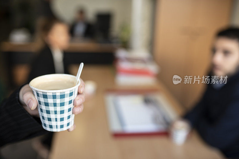 在办公室里，一只手拿着一杯热咖啡带走，在办公室喝咖啡休息一下