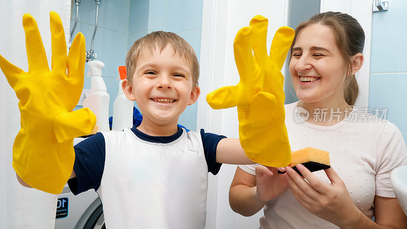微笑的蹒跚学步的小男孩戴着黄色橡胶手套，在做家务和打扫房间的时候大笑