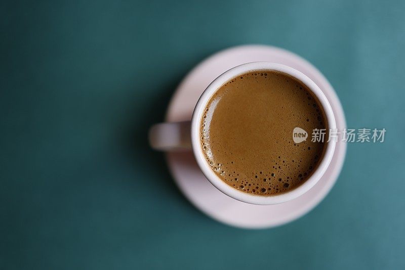 土耳其咖啡与大量的泡沫，在一个粉红色的杯子里，在一个深绿松石绿色的背景，蓝绿色的背景，特写