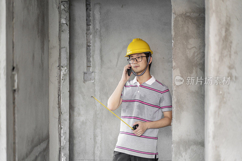 亚洲男性工程师使用电话和工作与头盔在翻新工地