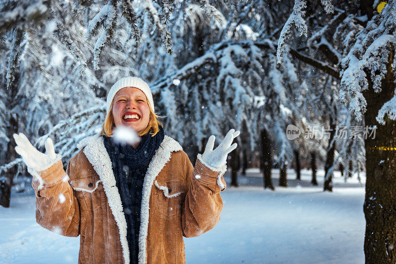 一个漂亮的年轻女孩戴着针织帽在冬天的森林里抛掷雪