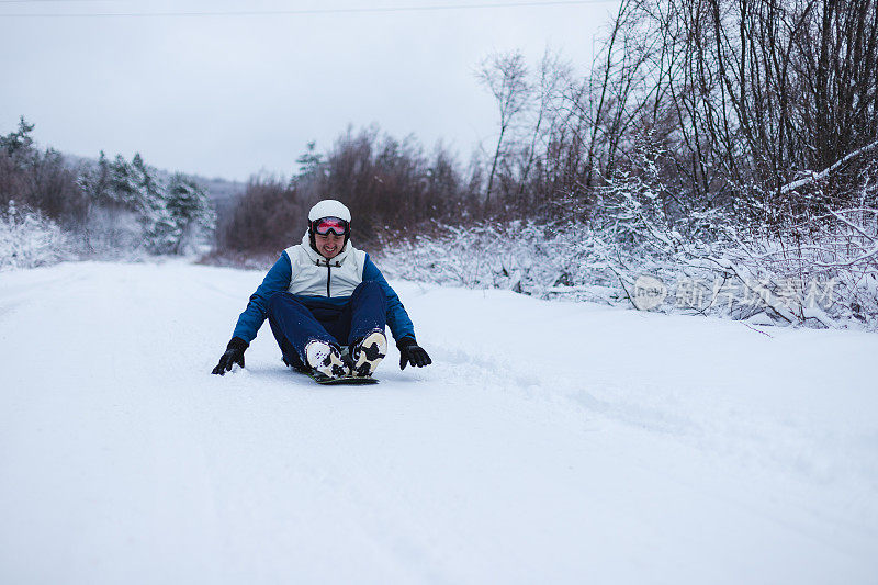 身穿蓝色服装的年轻男性滑雪板选手正坐在滑雪板上滑下山坡