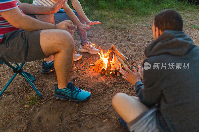 三个年轻朋友围在户外篝火旁暖手的特写