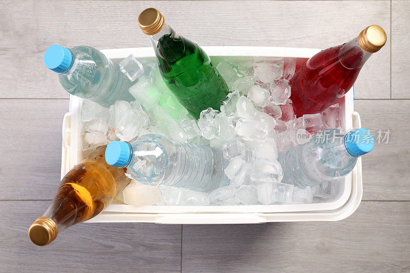 塑料冷盒装满冰块和提神饮料在木地板上，俯视图
