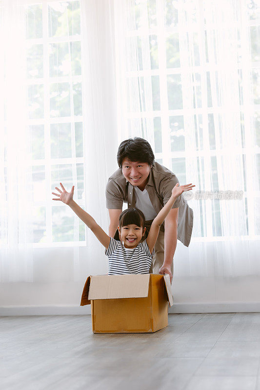 幸福的亚洲家庭在家里度过愉快的时光。父亲和可爱的女儿推着纸板箱在客厅周围的垃圾模型汽车的肖像。房地产，购买，家庭概念。