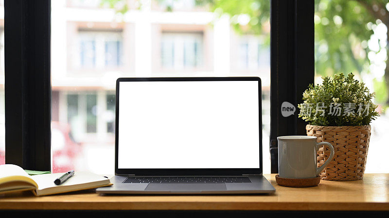 前视图笔记本电脑，咖啡杯，室内植物和笔记本在白色的桌子上。舒适的工作场所。