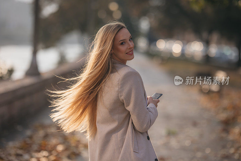 微笑的年轻女子在街上使用智能手机