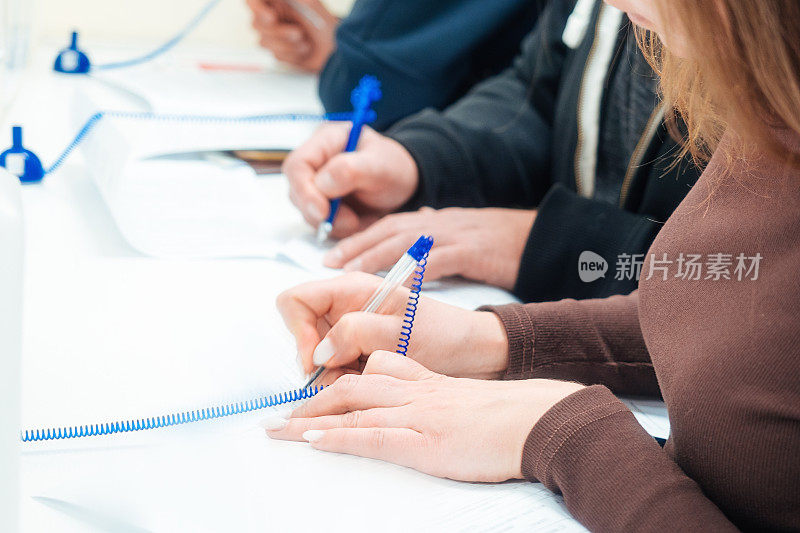 妇女在桌子上填写空白申请表或签署合同。手里拿着近距离的自来水笔。几个人同时用笔在纸上填写数据。