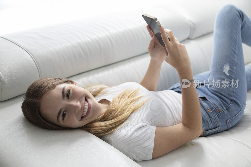 十几岁的女孩拿着手机躺在沙发上。