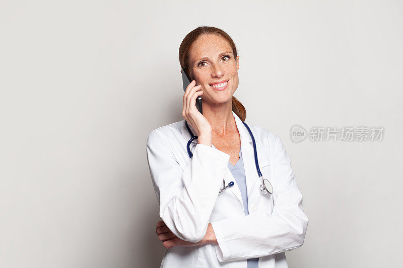 现代女性肖像快乐成功，有吸引力的成熟成年女医生，医生从业人员与智能手机在她的手中
