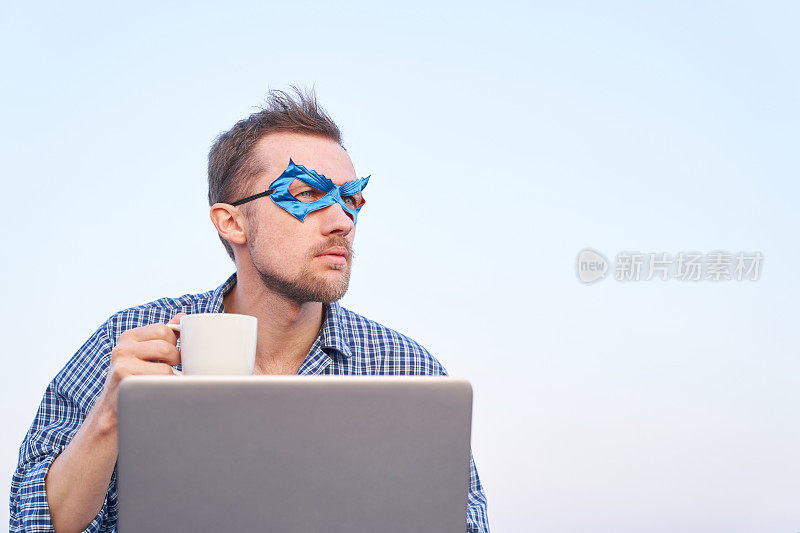 超级英雄电脑男戴着蓝色面具在户外用笔记本电脑拿着咖啡杯