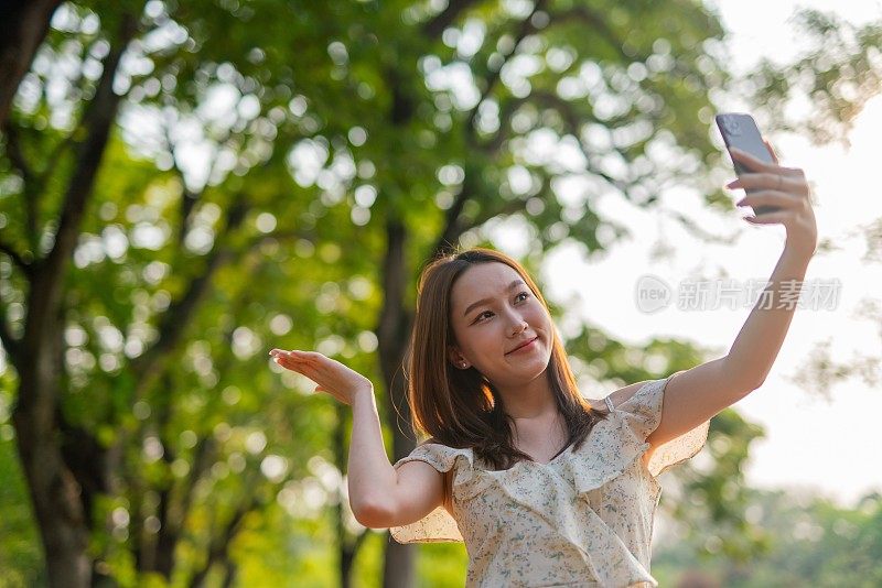 年轻的亚洲女子在公园用手机自拍。在郁郁葱葱的绿色森林里，美女视频通话