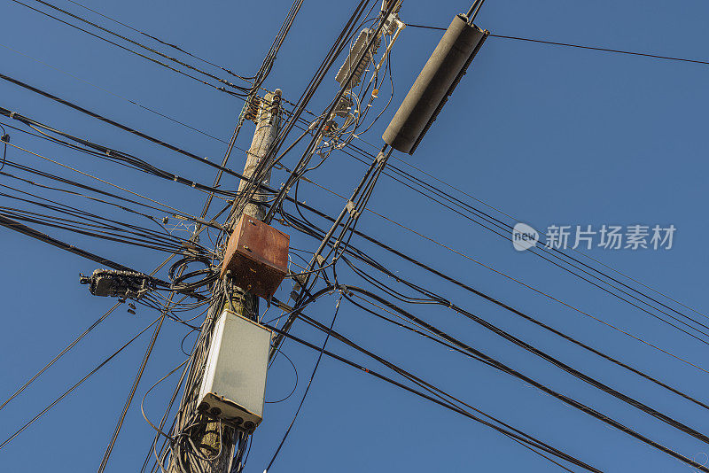 一个电线杆，上面有互联网和电视电缆、电话线和电线，衬着蓝天。
