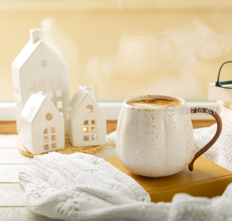 秋天的构图，一杯热咖啡，蜡烛，烛台，一个微型房子和一件温暖的毛衣放在木桌上。应季，早晨热咖啡。放松和静物概念。舒适的室内装饰