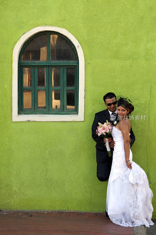 新婚夫妇靠在绿色的墙上