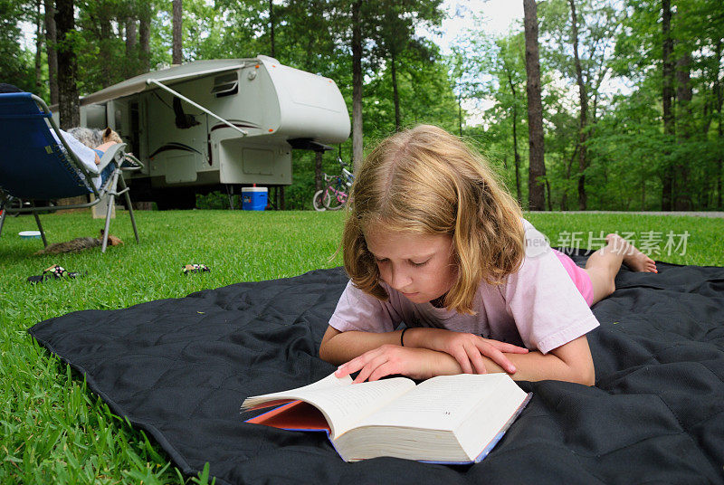 小女孩在营地的地上看书