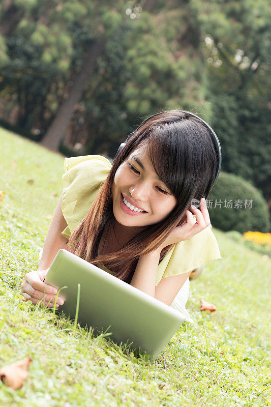 亚洲女学生在草地上用写字板听音乐