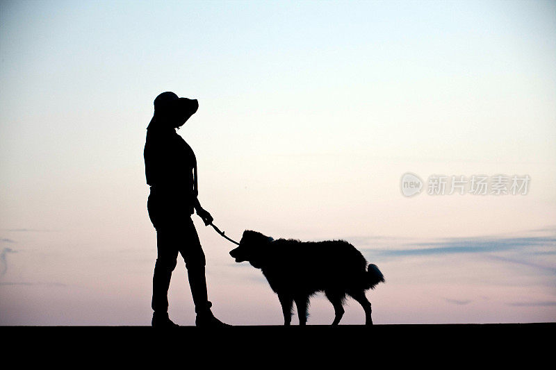 成熟的西班牙妇女和牧羊犬剪影日落