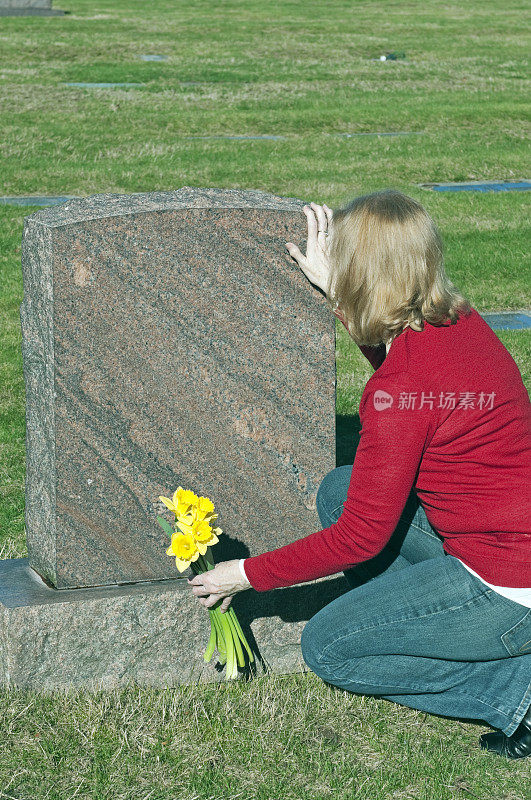 一个女人拿着鲜花跪在墓地的墓碑前