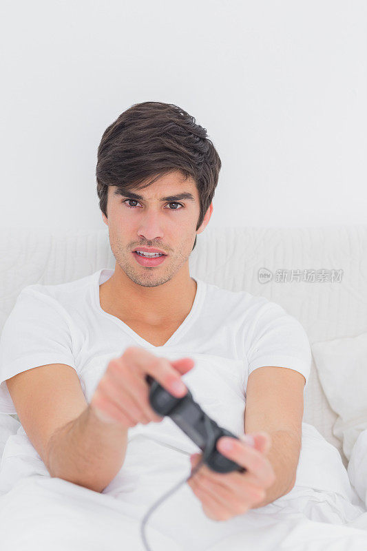 英俊的年轻人坐在床上玩电子游戏