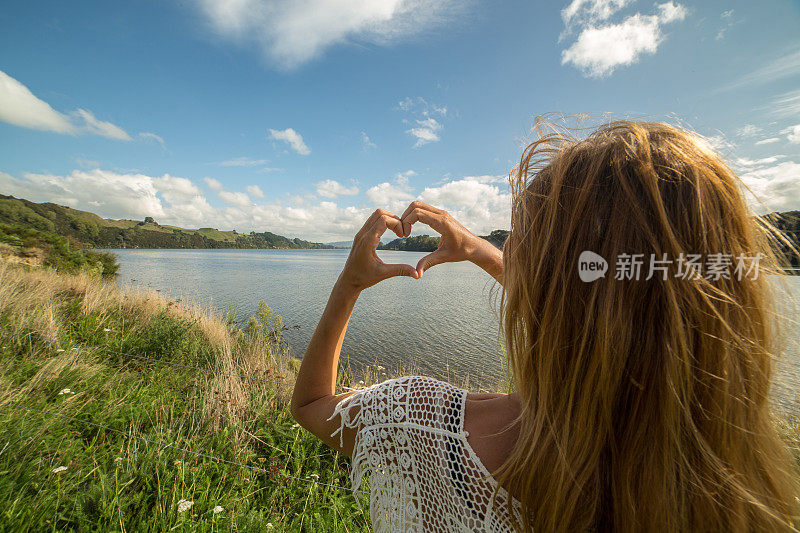 一个年轻女子在湖边做了一个心形的手指架