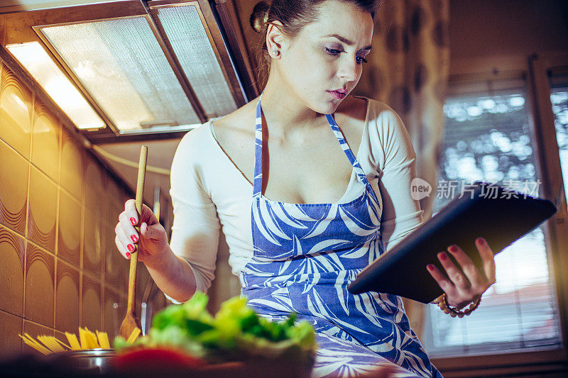 美丽的年轻女子在数字平板电脑上阅读食谱