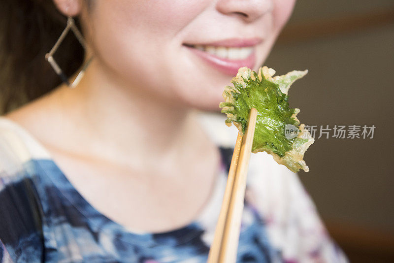 一名日本妇女微笑着用筷子吃荨麻天妇罗