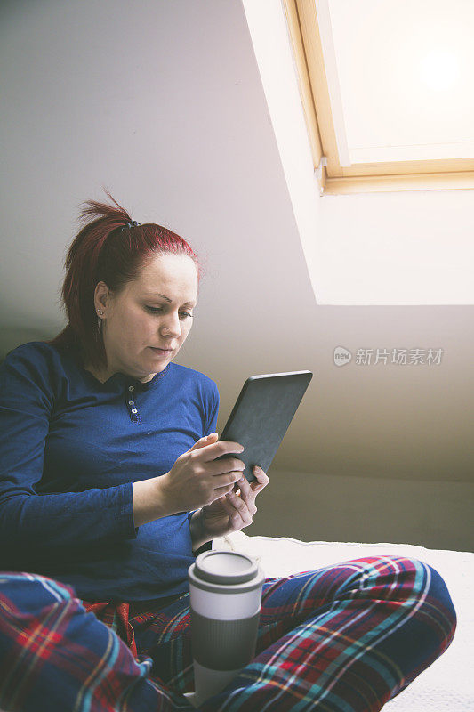 穿着睡衣的女人在床上使用电子平板电脑