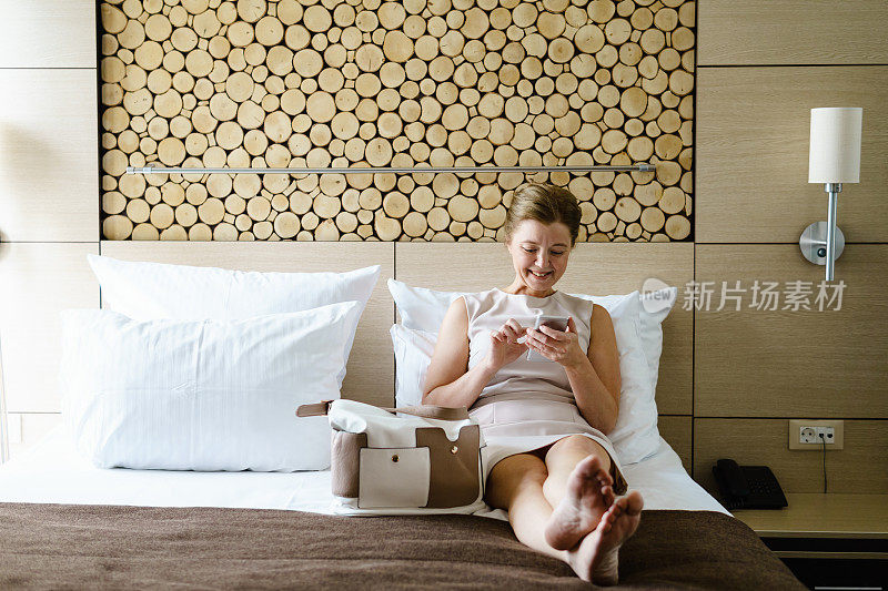 成熟的女商人在酒店房间里使用智能手机。