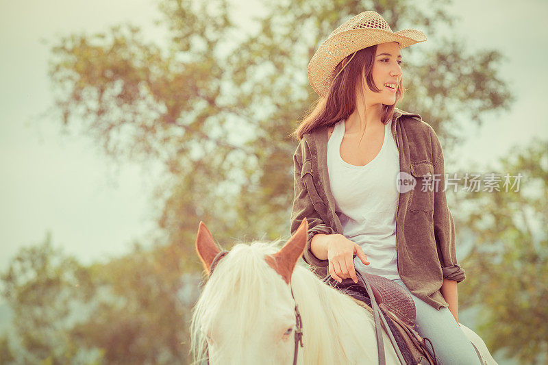 戴牛仔帽的年轻女子骑着白马在户外
