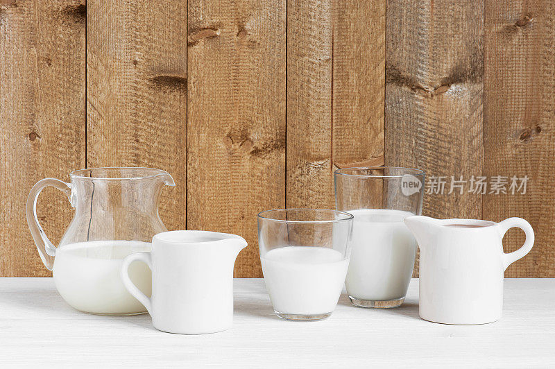 木桌上放着各种盛牛奶的壶和玻璃杯