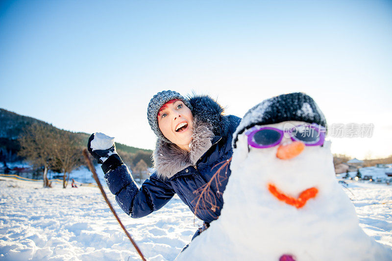 一个成年女人在打雪仗时躲在雪人后面