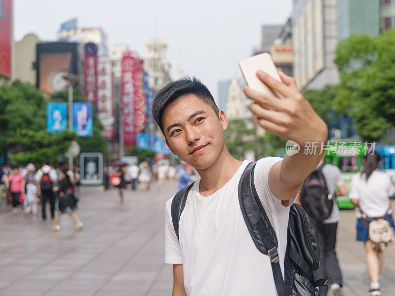 户外肖像的年轻亚洲男子用他的智能手机自拍照片与上海外滩的背景。