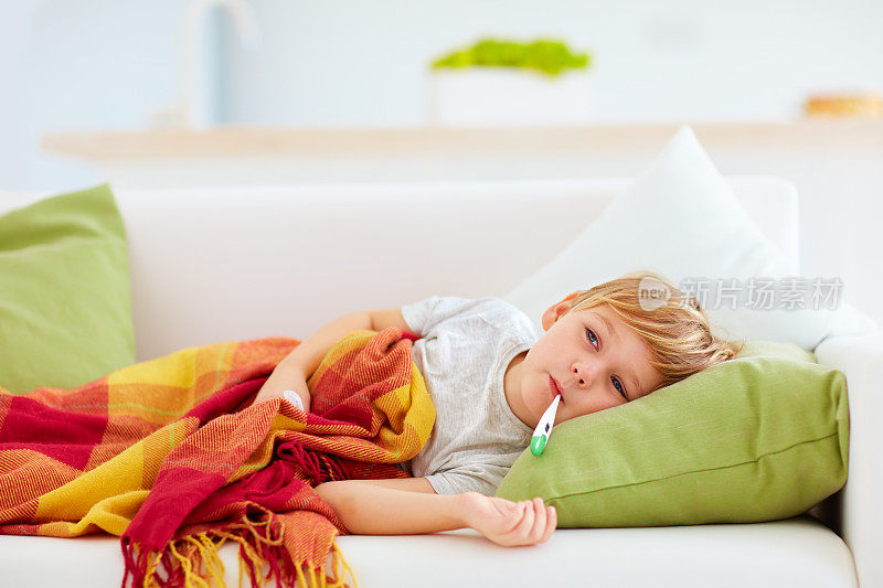 生病的孩子流鼻涕和发烧热躺在家里的沙发上