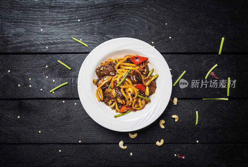 乌冬面条与肉和蔬菜在一个白色的盘子在黑色的木制背景。用筷子和酱。炒锅。