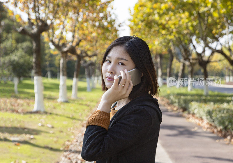年轻的亚洲孕妇在公园里打电话