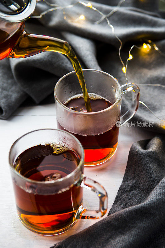 将红茶从透明茶壶中倒入杯子中。冬天家里的概念