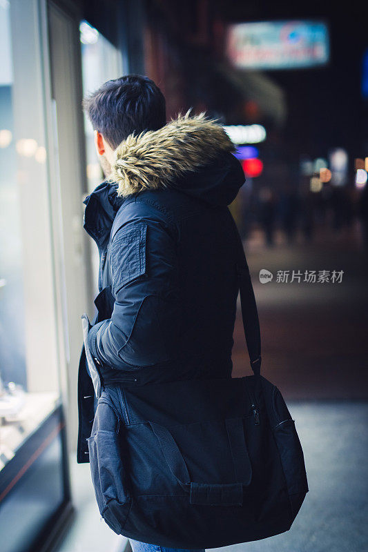 一个年轻人晚上在城市里看商店的橱窗