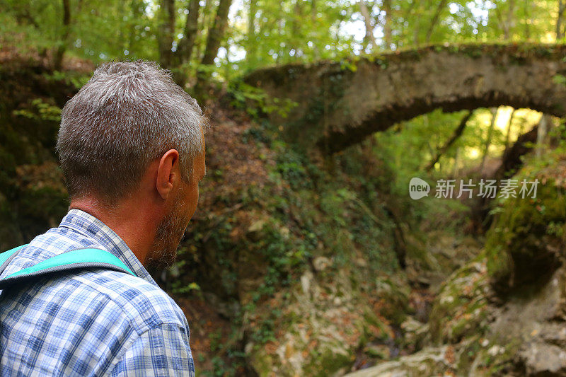 成年男子徒步旅行在美丽的自然景观与小溪流在森林和老废弃的石桥上面