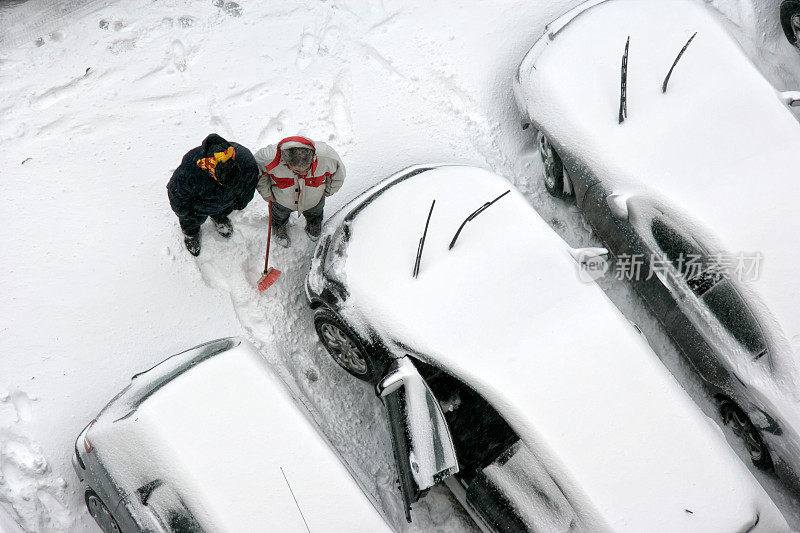 在被雪覆盖的停车场，两个人正在清理结冰的汽车