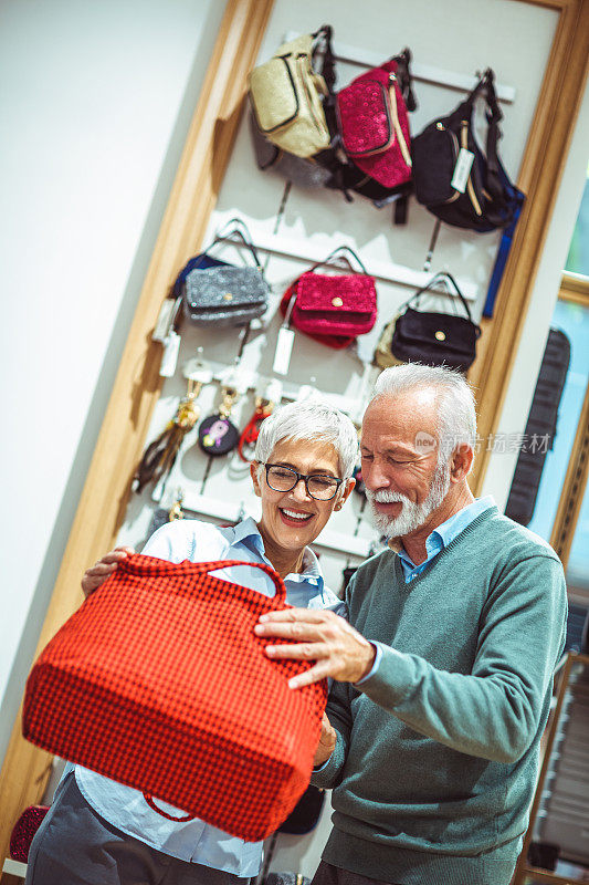 一对浪漫的老夫妇在购物袋和饰品店一起挑选红色格子钱包