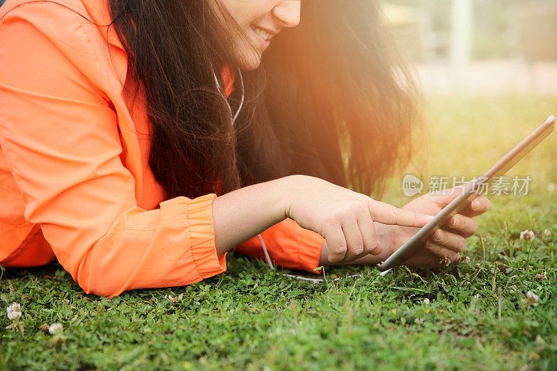 快乐的年轻女人躺在草地上，使用数字平板电脑