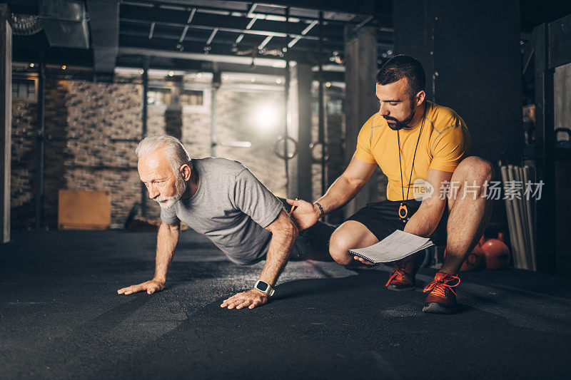 一个活跃的老人在健身房前和教练一起做俯卧撑