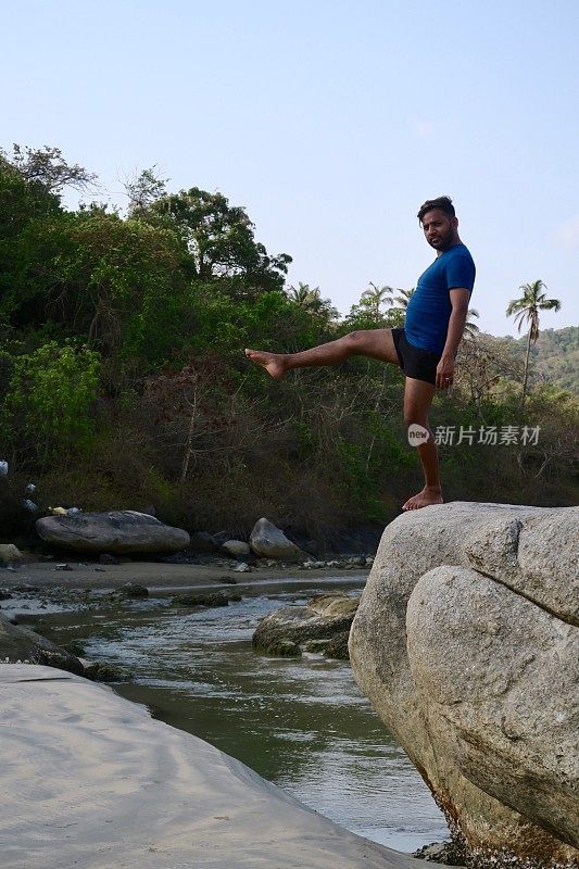 印度男子练习站立平衡单腿瑜伽姿势，在岩石上，水的边缘，帕洛伦海滩，果阿，印度